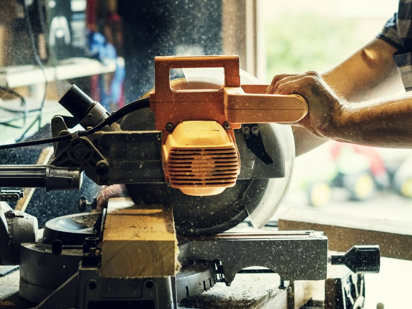 Worker cutting wood with circular saw creating dust in workshop